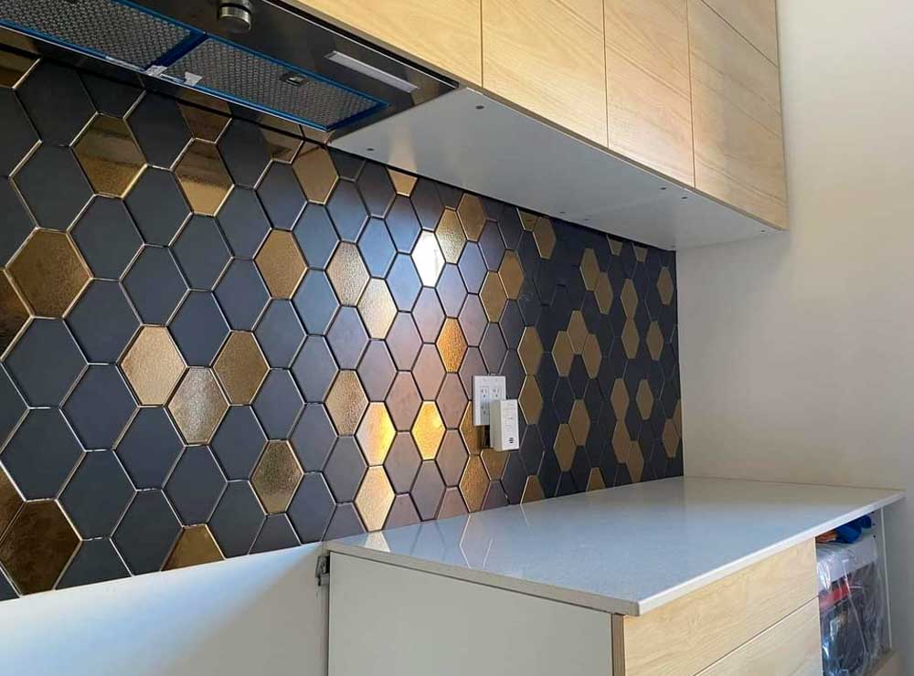 close-up of an elegant black gold hexagon pattern kitchen backsplash with electrical sockets, and white quartz countertop