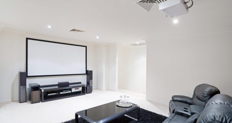 basement multimedia room, white painted walls, black sofa, carpet and table, with large viewing white screen and audio system
